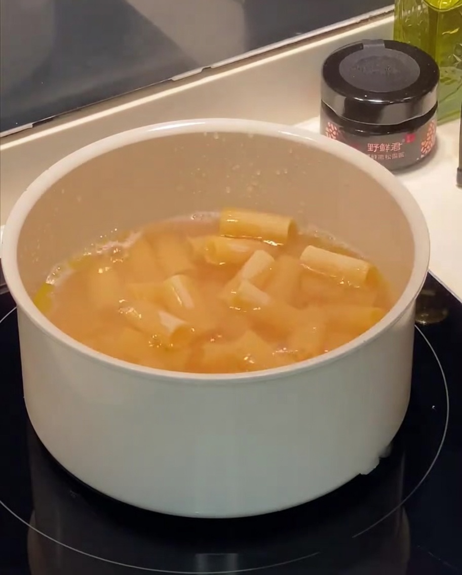 Rigatoni che bollono in una pentola dacqua con bolle visibili e gocce dolio in superficie.