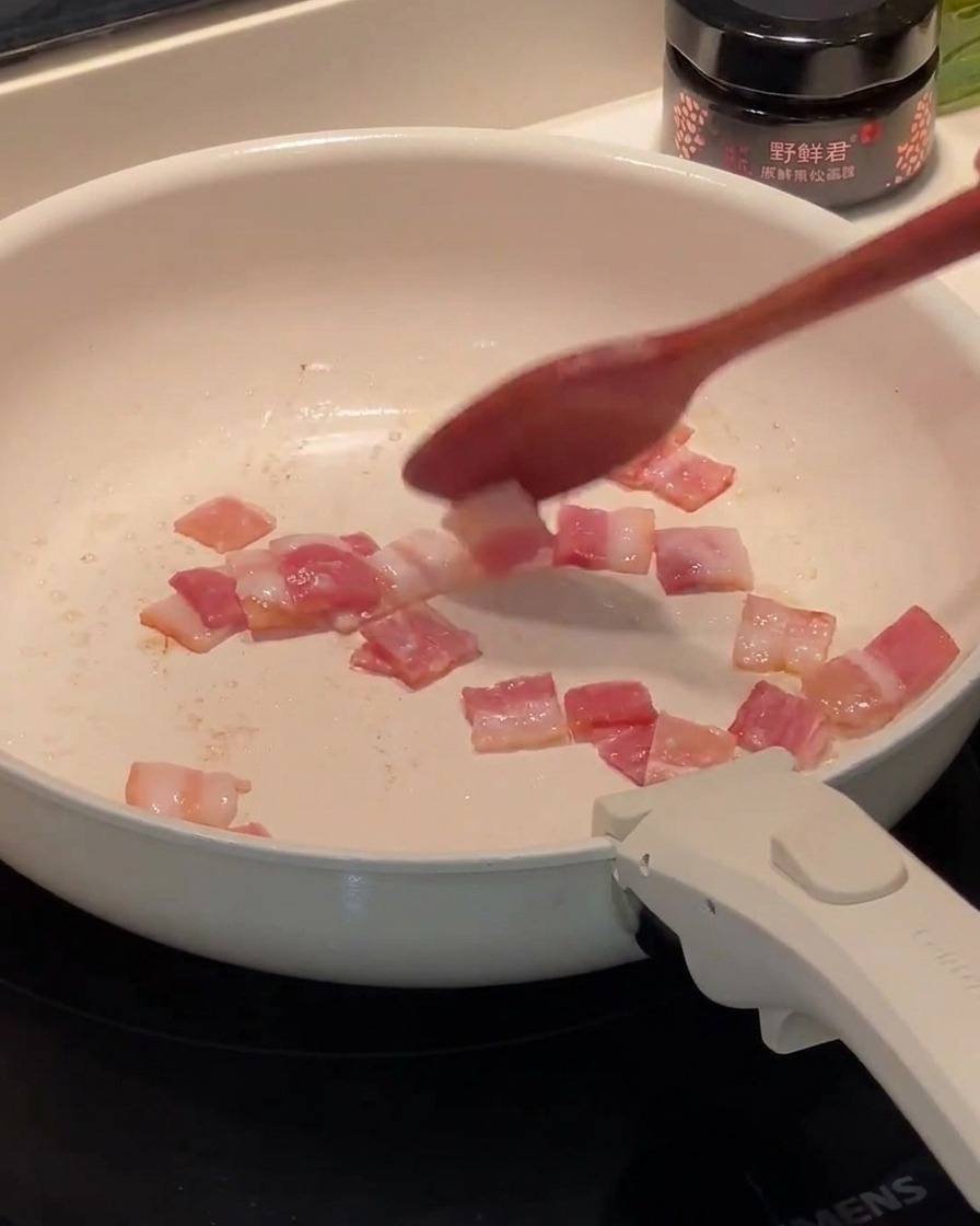 Bacon a pezzetti che frigge in una padella, con il grasso che inizia a sciogliersi sul fondo.