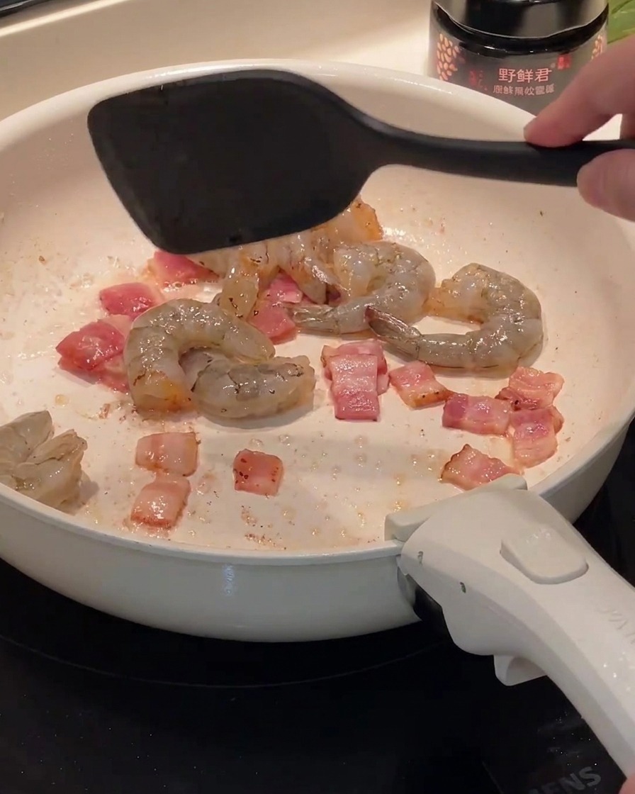 Gamberi crudi aggiunti in padella insieme al bacon rosolato.