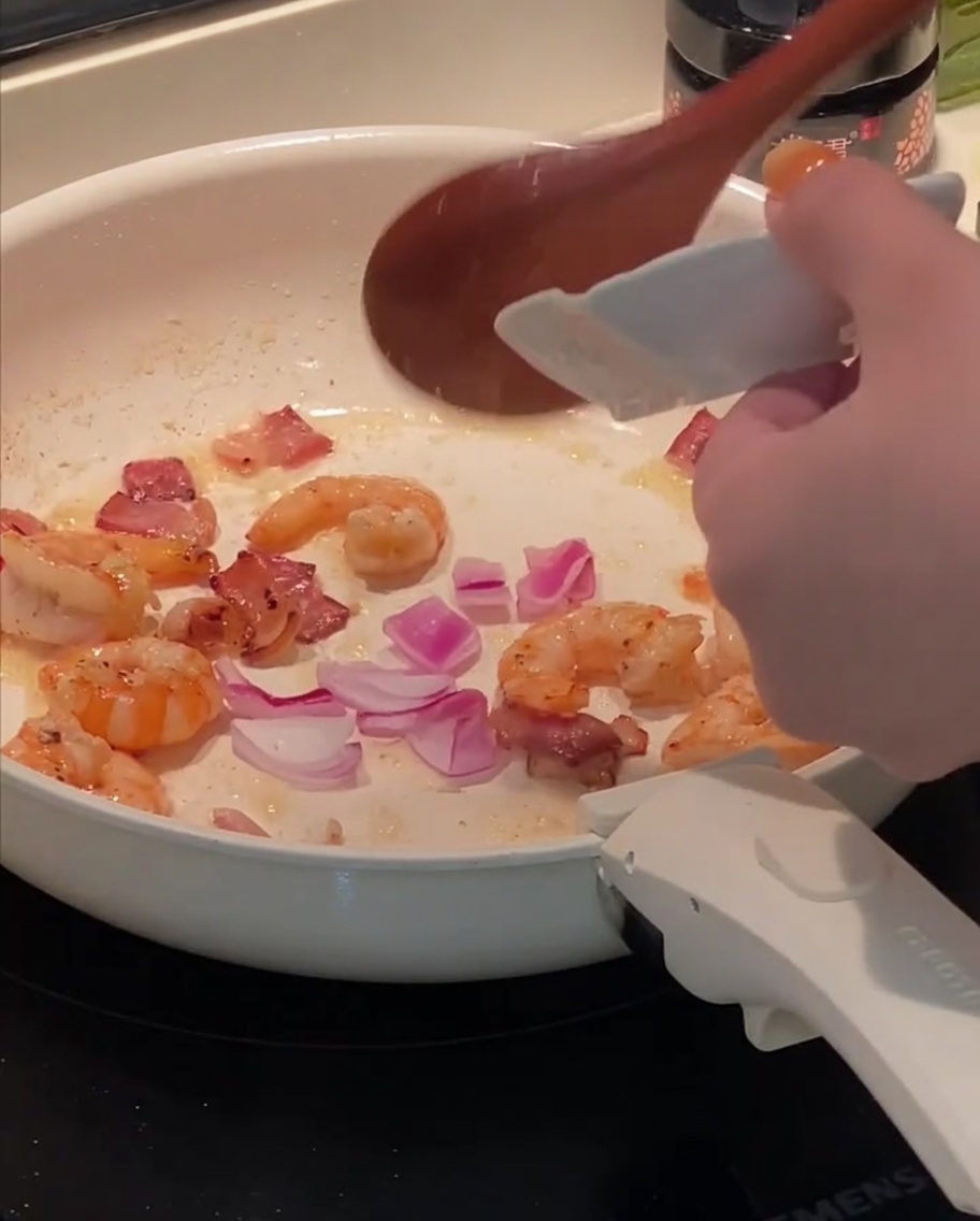 Cipolla tritata aggiunta in padella con gamberi e bacon.