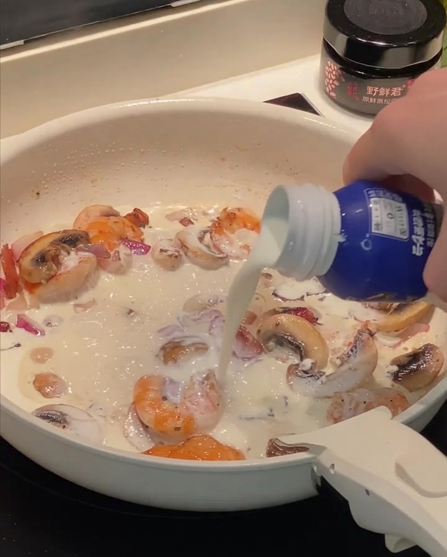 Panna e latte versati nella padella con gamberi, bacon e funghi.