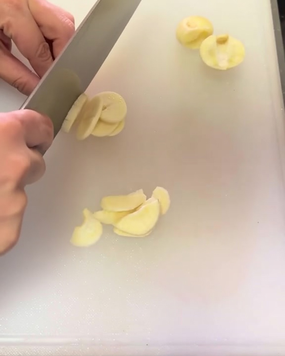 Spicchi daglio affettati sottilmente sparsi su un tagliere bianco.