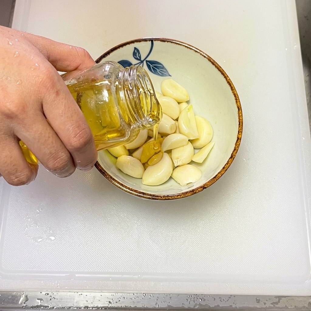 Olio doliva versato in una ciotola contenente aglio fresco affettato.