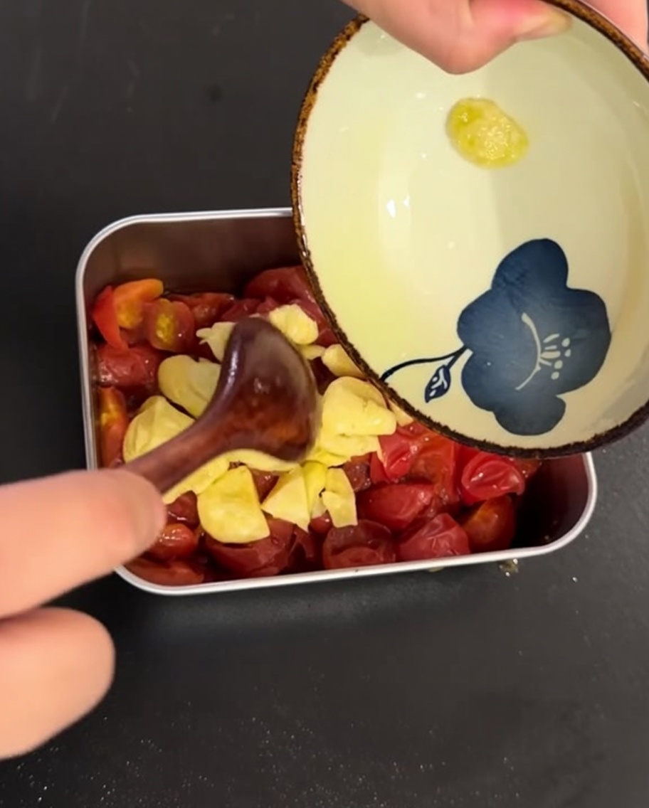 Lolio infuso allaglio versato sopra i pomodorini cotti in un piatto di metallo.