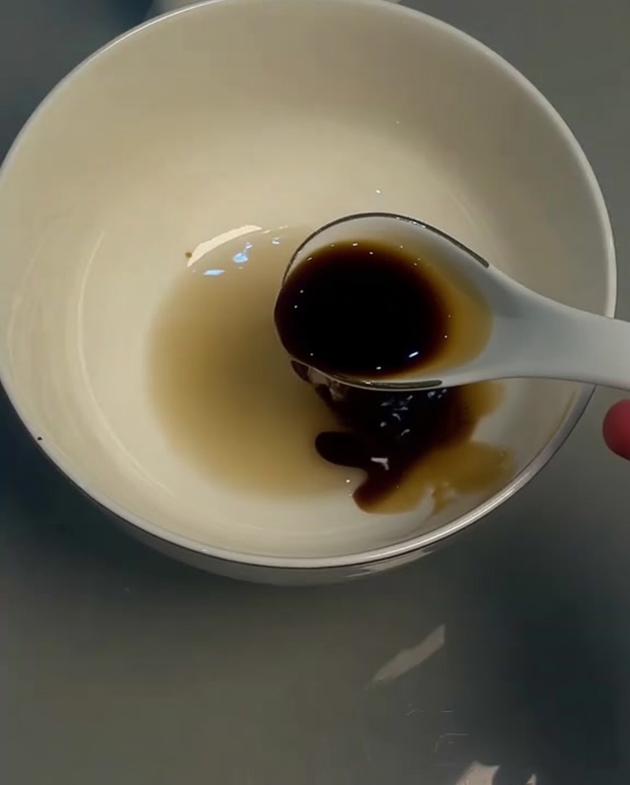 Salsa di soia chiara in una ciotola bianca mescolata con un cucchiaio.