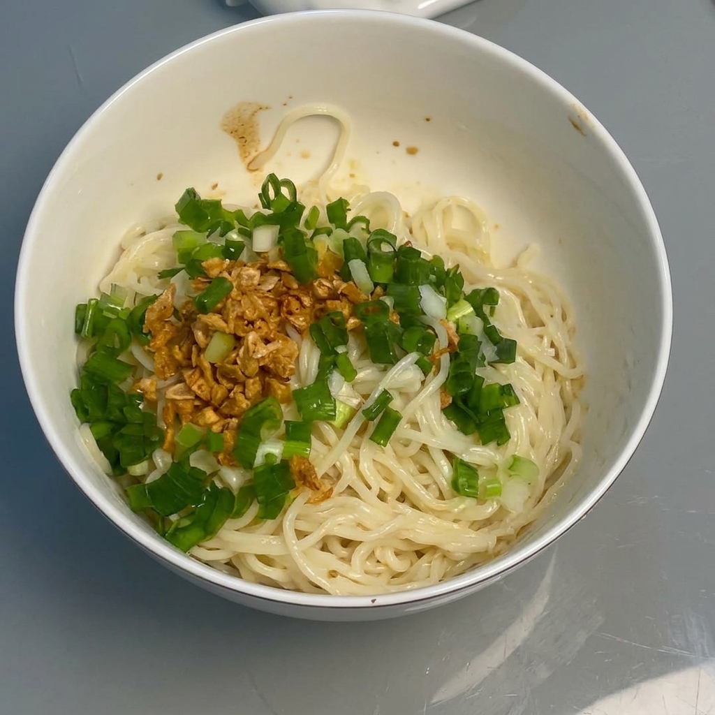Noodles mescolati con salsa, aglio e cipollotti usando le bacchette.