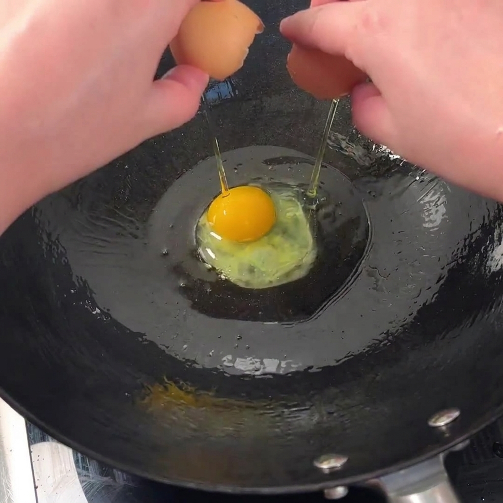 Due uova fresche che si rompono e sfrigolano in un wok caldo e oliato per ottenere bordi croccanti.