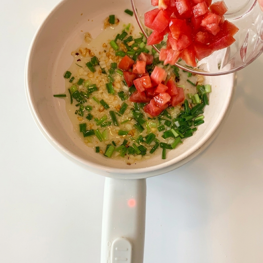 Pomodori a cubetti aggiunti nel pentolino con aglio e cipollotti.