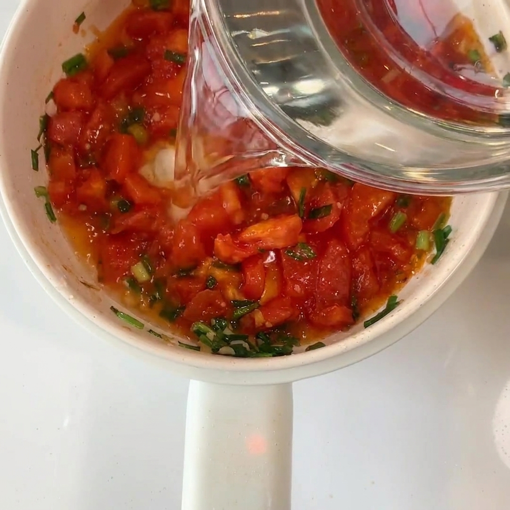 Acqua versata da una ciotola di vetro nel pentolino con i pomodori.