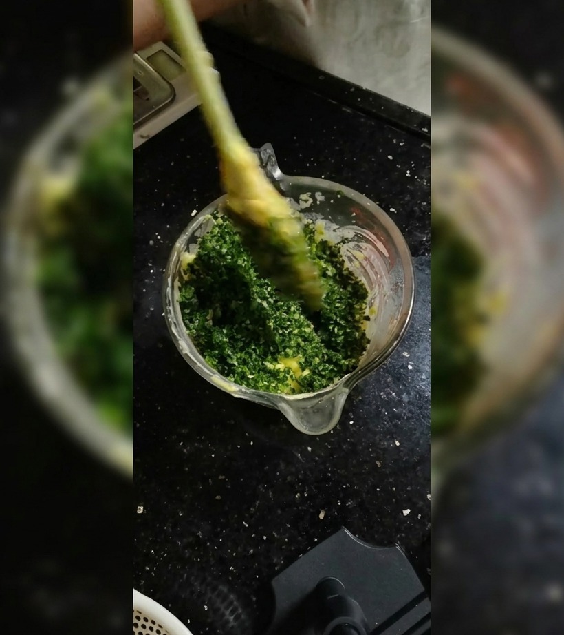 Una spatola in silicone amalgama le erbe al burro morbido in una ciotola di vetro.