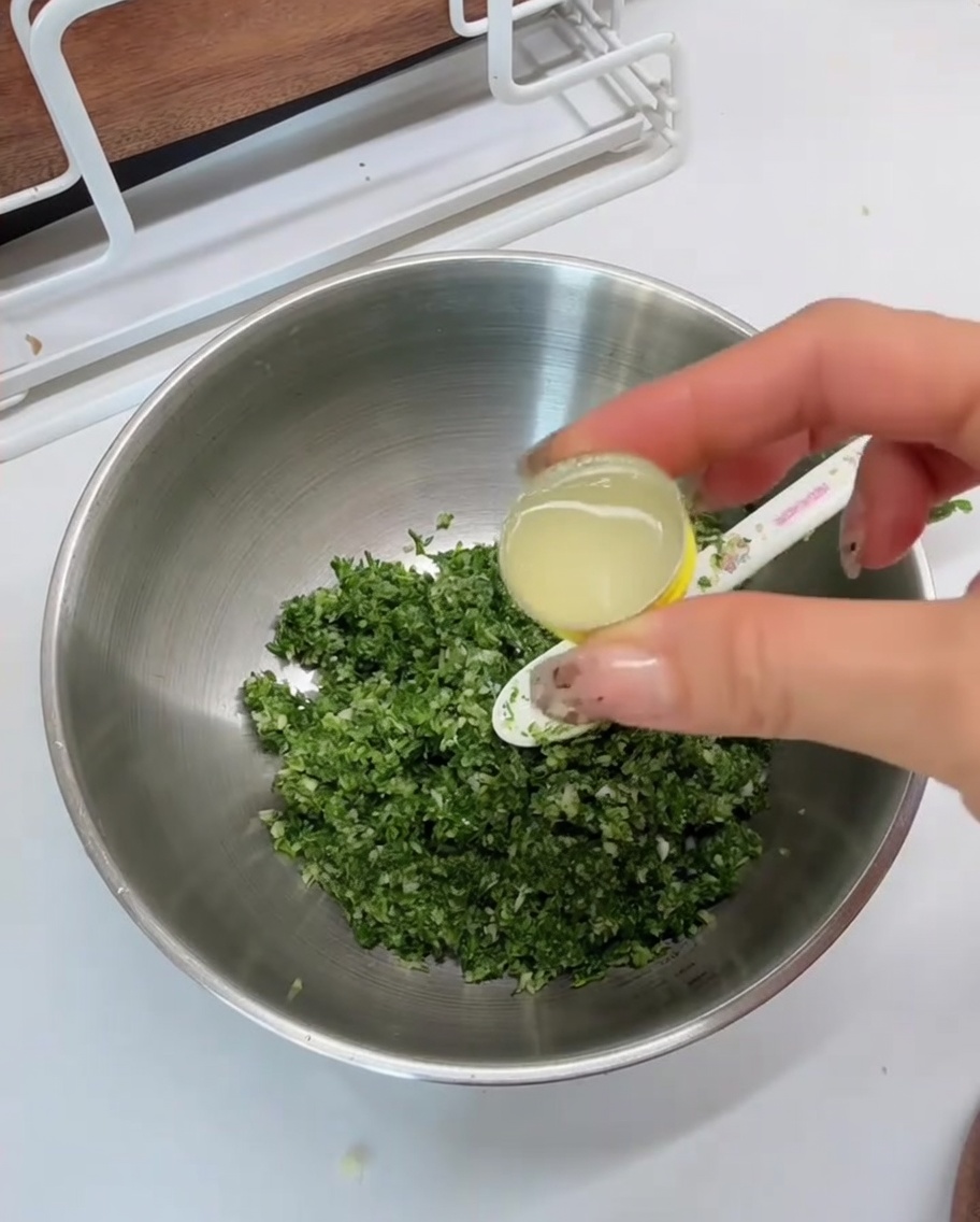 Succo di limone versato da un piccolo cucchiaio dosatore in una ciotola di metallo contenente il trito verde.