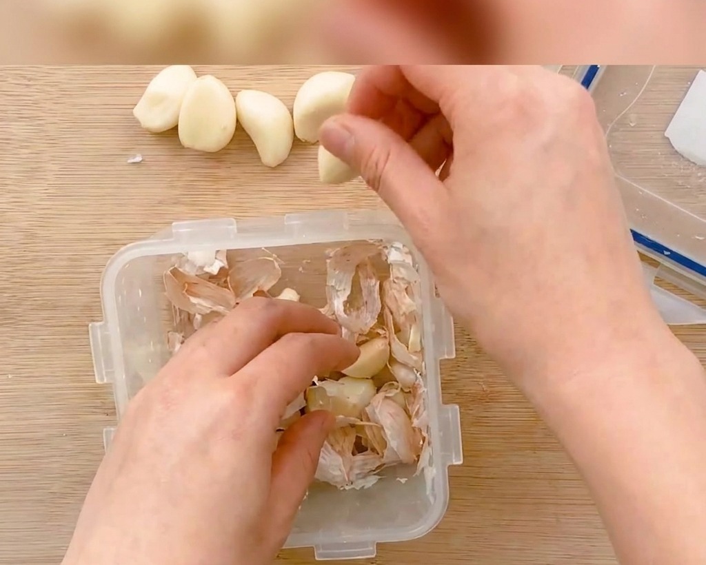 Spicchi daglio sbucciati e tagliati a fettine sottili su un tagliere di legno.