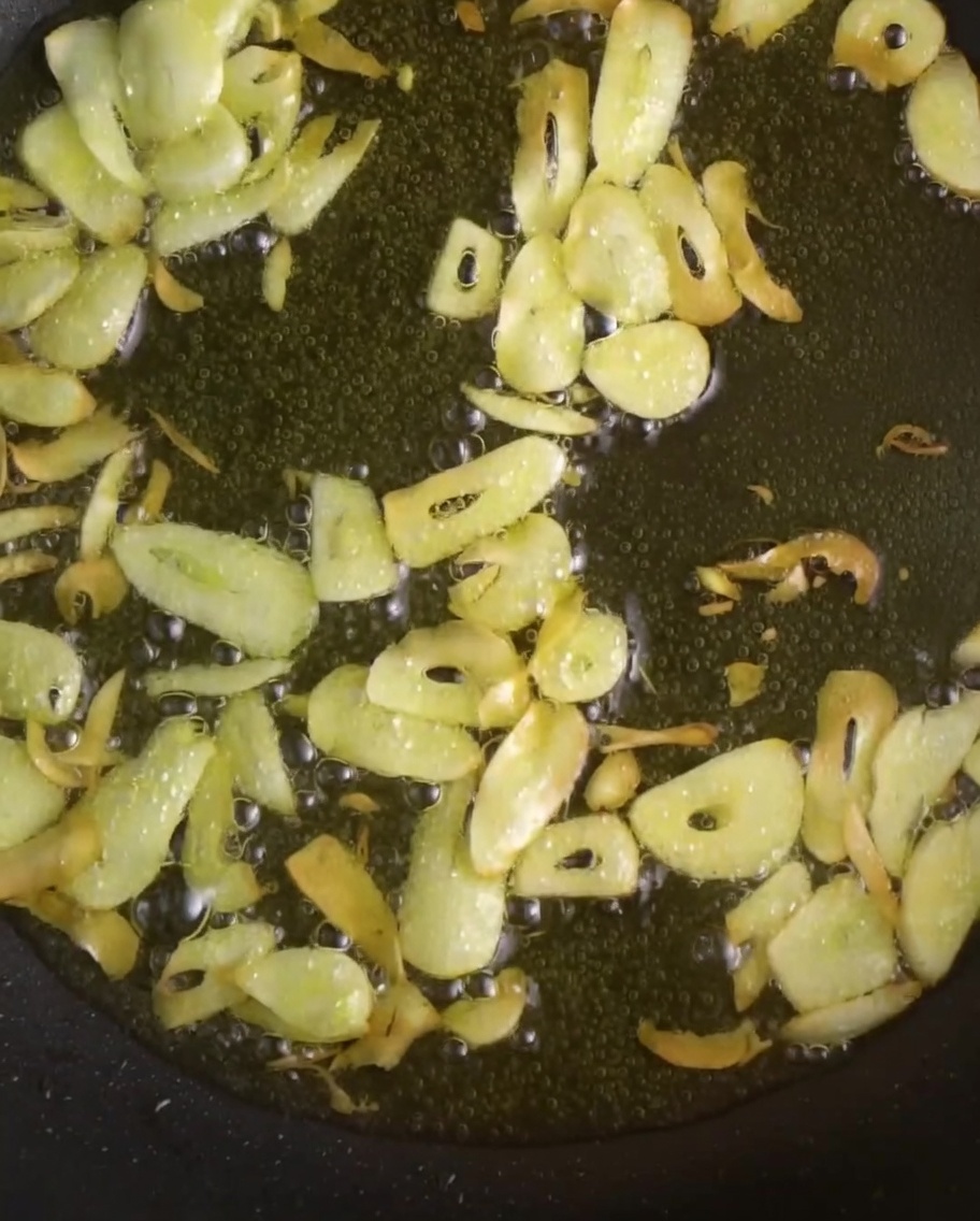Aglio affettato e peperoncini rossi vibranti che friggono nellolio in padella.