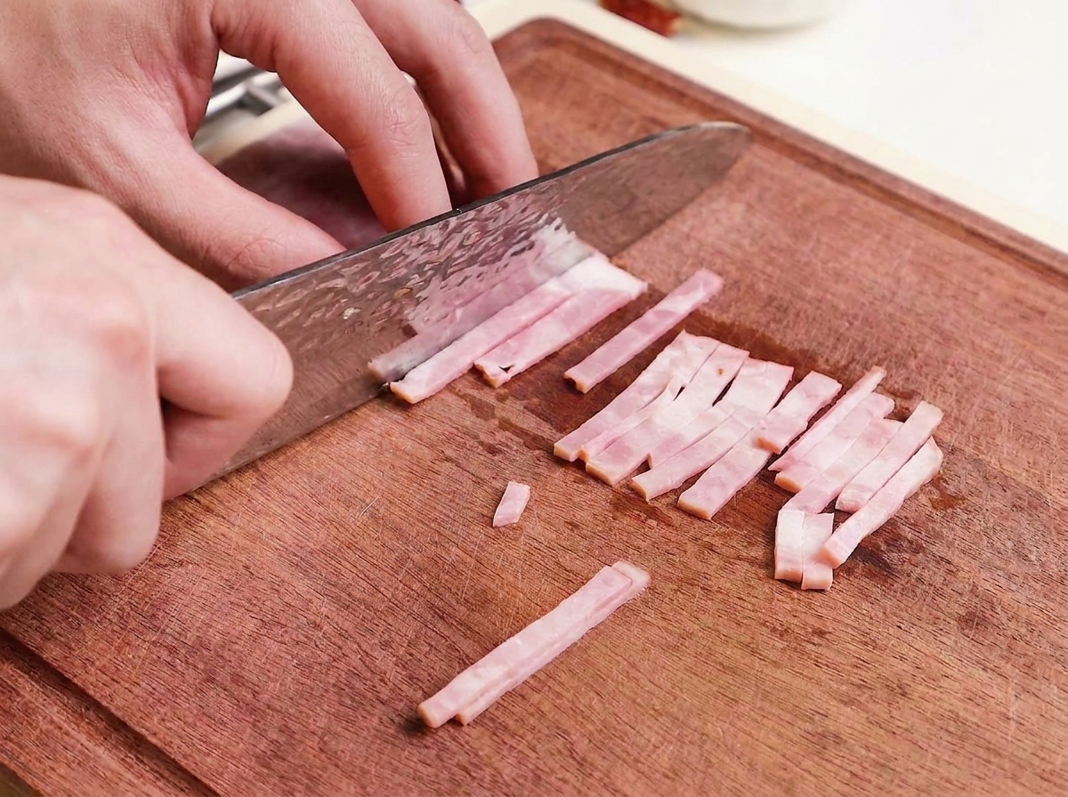 Strisce sottili di pancetta cruda tagliate su un tagliere di legno.