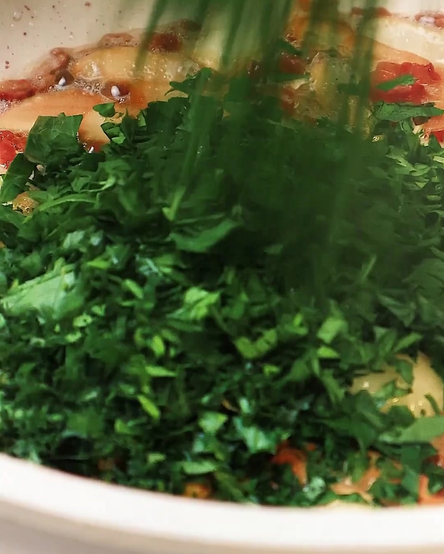 Prezzemolo tritato aggiunto alla padella contenente aglio e pancetta, mescolando leggermente per amalgamare.