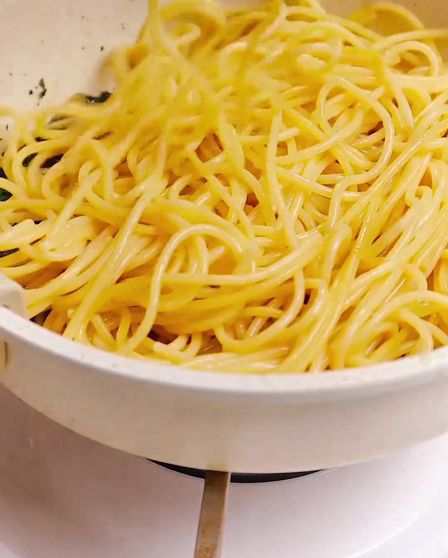 Spaghetti cotti saltati in padella con una miscela di pancetta, aglio e aromi usando delle pinze.