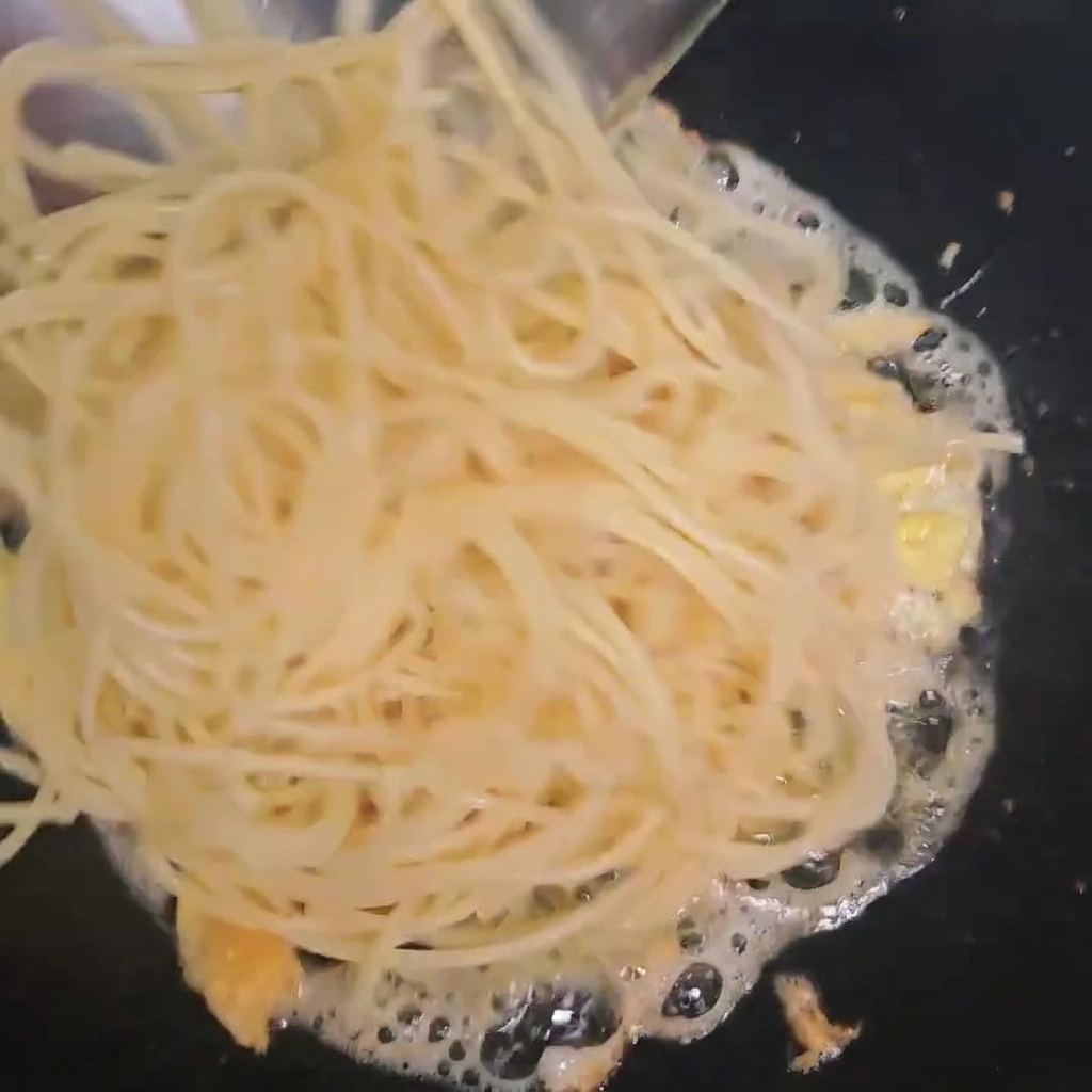 Spaghetti cotti aggiunti nel wok con le uova fritte.