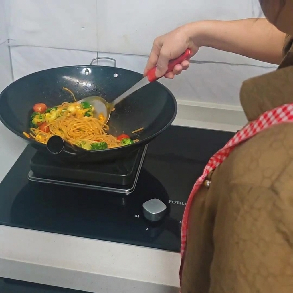 Una persona che usa una spatola per saltare spaghetti, broccoli e uova nel wok.