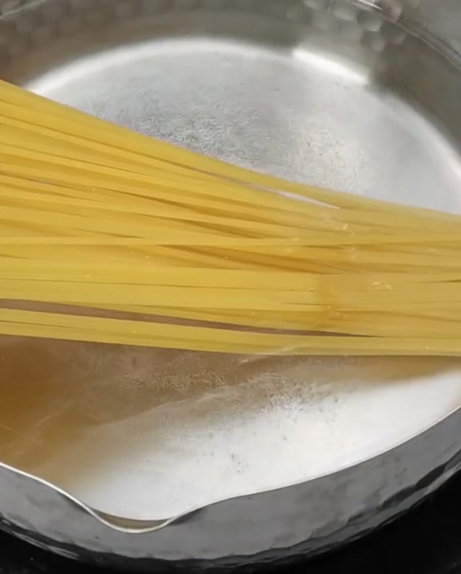 Pasta lunga immersa in una pentola dacciaio con acqua bollente.