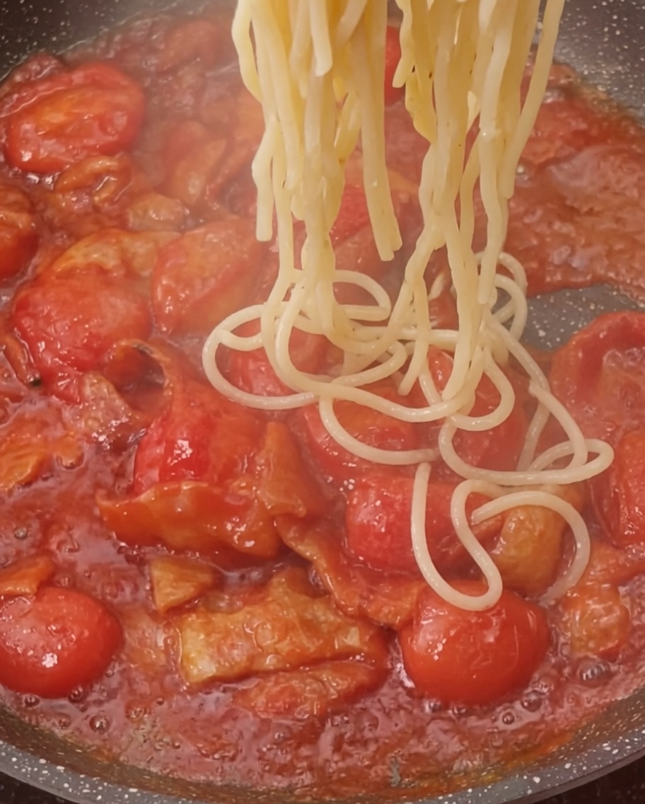 Pasta cotta aggiunta in padella con il sugo di pomodoro e pancetta.