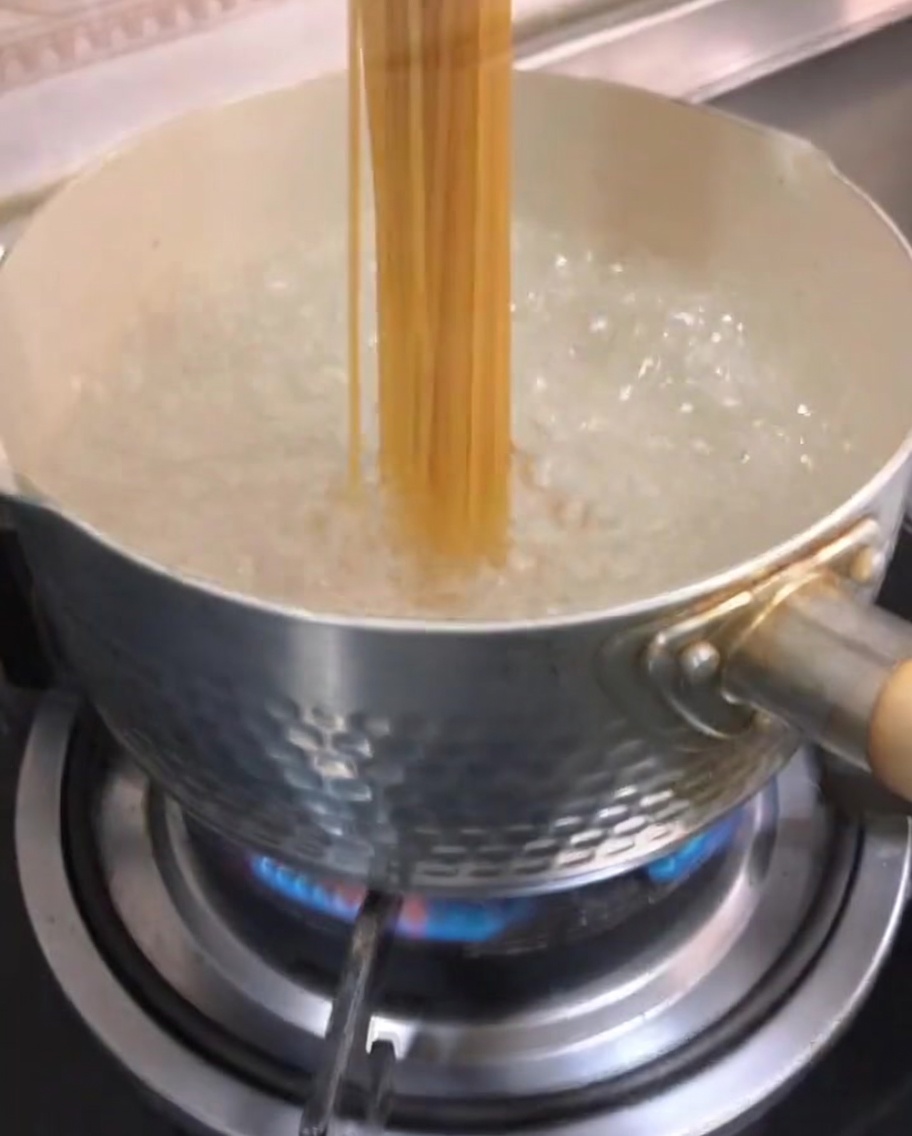 Spaghetti crudi immersi in acqua bollente in una pentola.