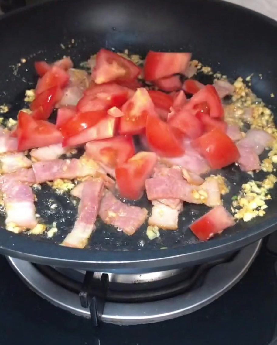 Pezzi di pomodoro rosso fresco appena tagliati aggiunti al bacon e allaglio che rosolano in una padella.