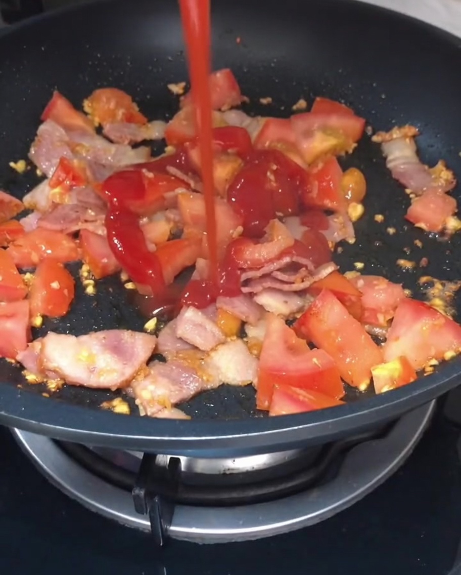 Ketchup e salsa di soia chiara versati sul composto di pomodoro e bacon saltato in padella.