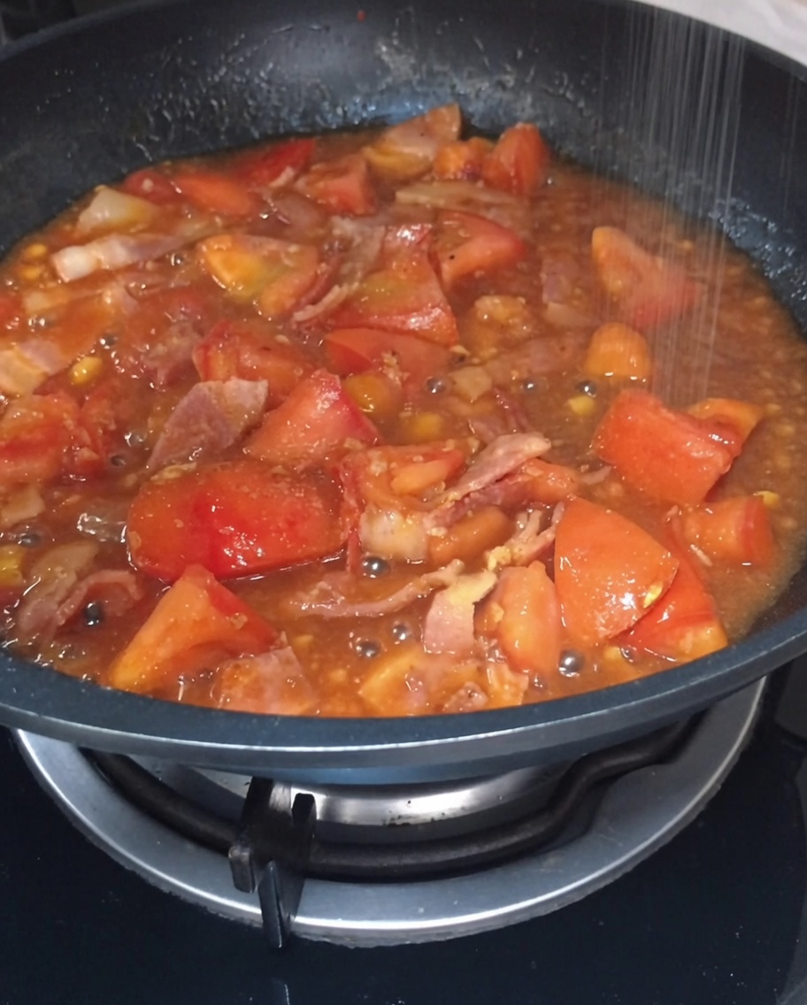 Sale e zucchero spruzzati nel sugo di pomodoro e bacon che bolle nella padella.