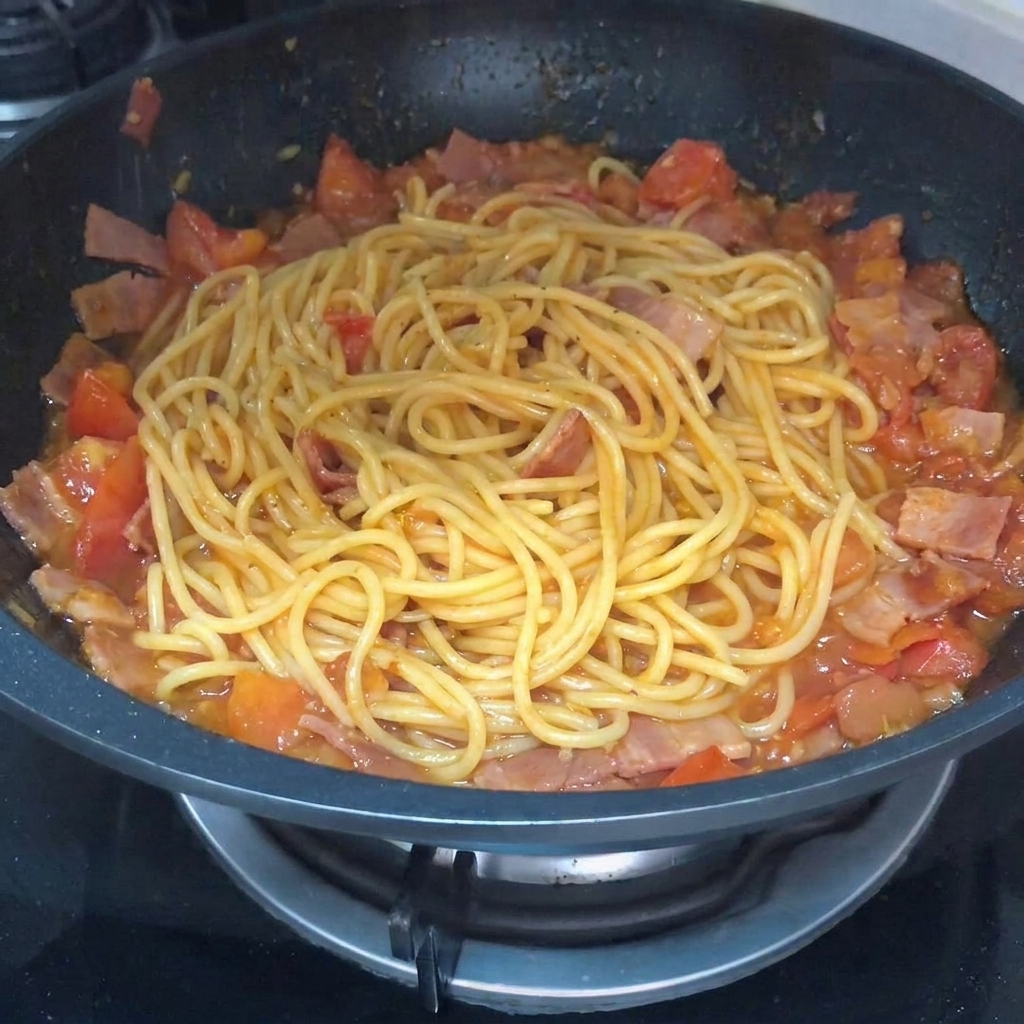 Primo piano di pasta saltata in padella con sugo di pomodoro e bacon, con pepe nero spolverato sopra.