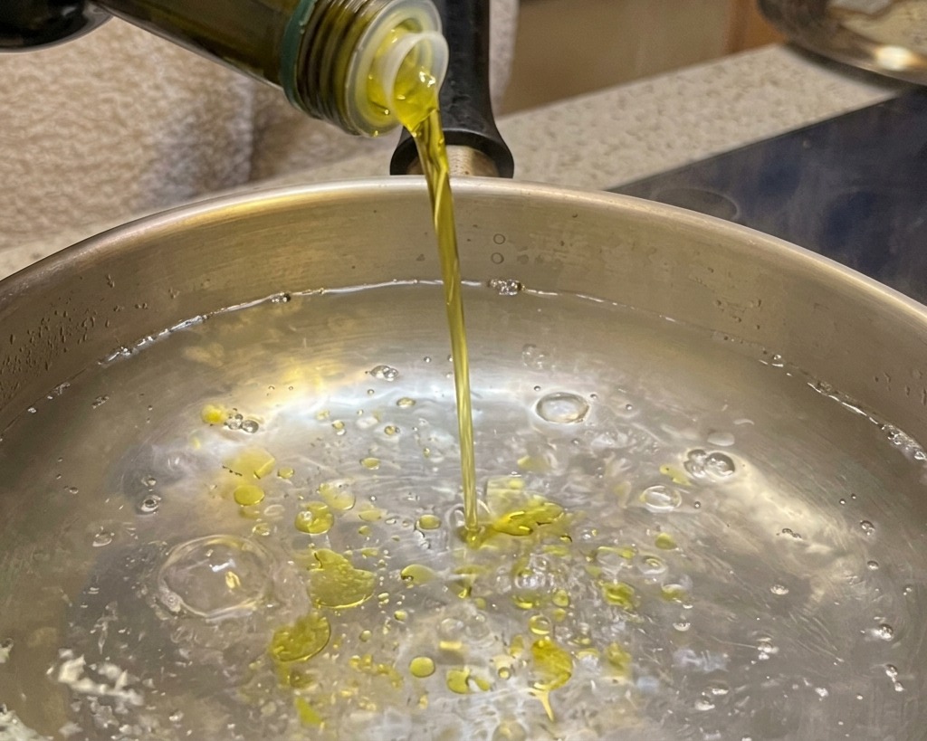Versare dellolio doliva in una pentola di acqua bollente.