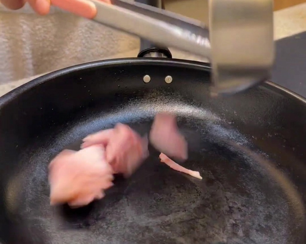 Aggiungere i pezzetti di bacon in una padella nera per friggerli.