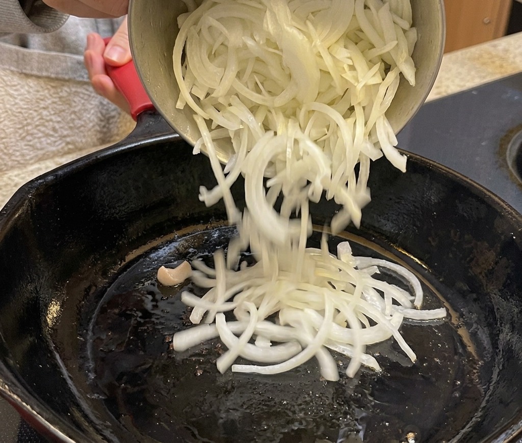 Versare cipolle affettate sottilmente in una padella nera.