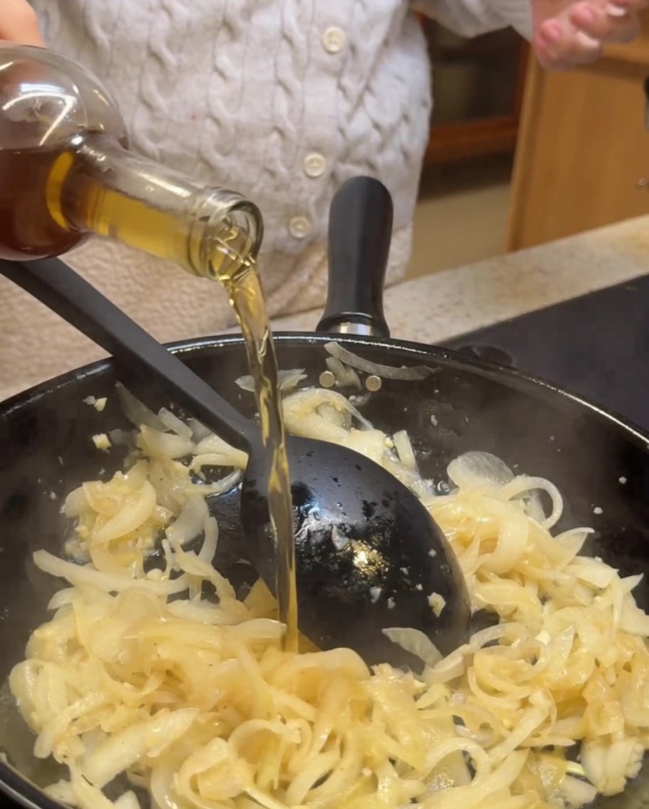 Vino bianco e aceto balsamico versati in una padella con cipolle e aglio saltati.