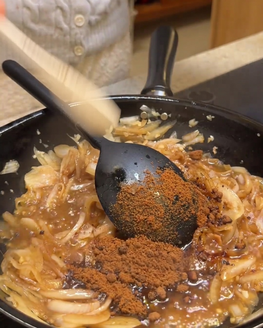 Zucchero di canna cosparso in una padella contenente cipolle e aromi saltati.