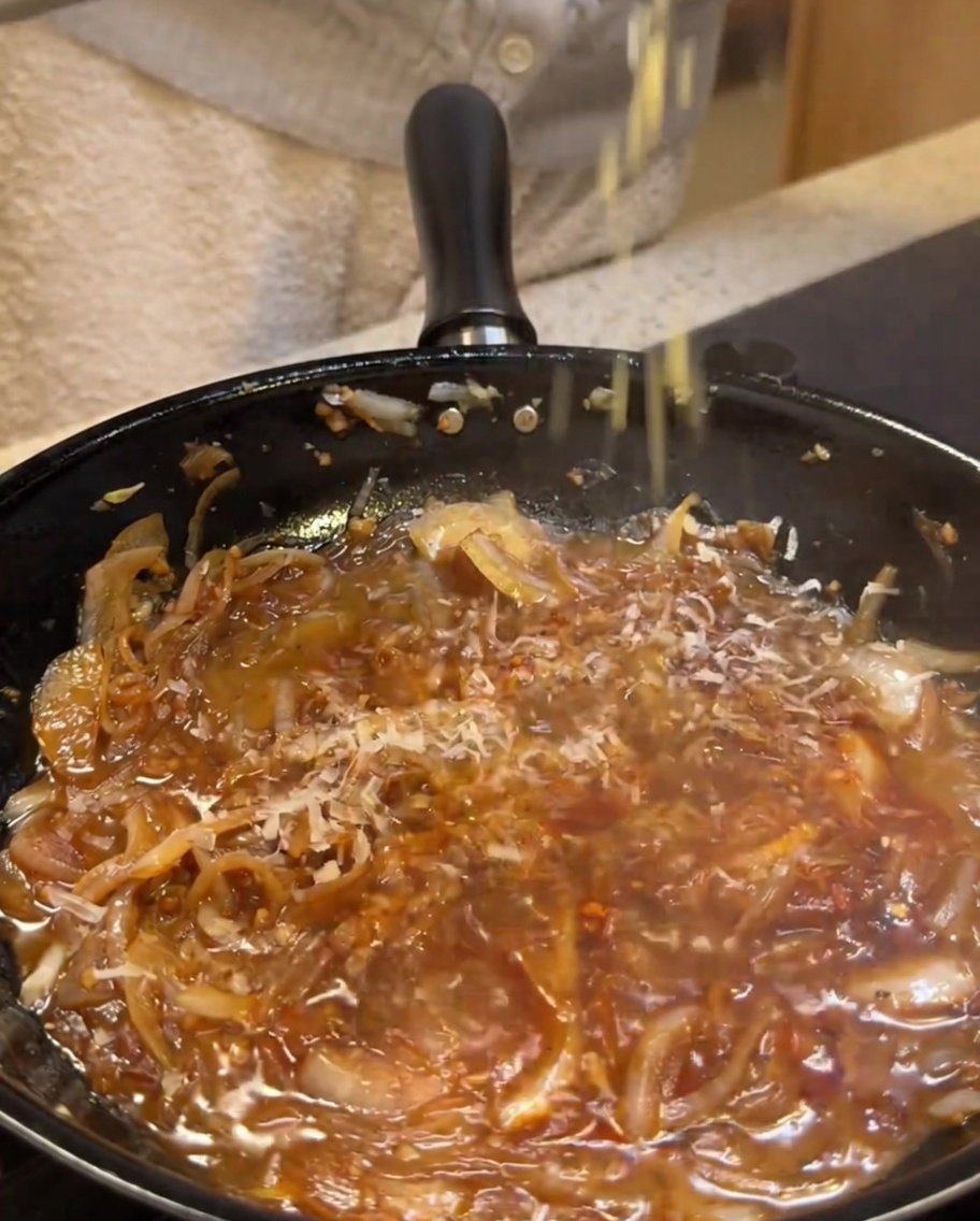 Parmigiano grattugiato direttamente in una base di salsa cremosa che sobbolle.