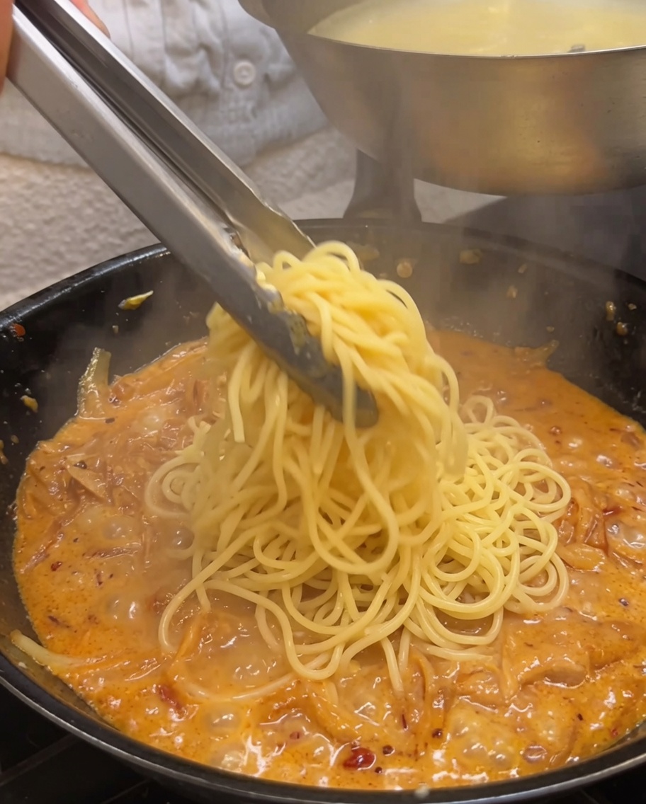 Spaghetti cotti saltati in una salsa cremosa alle cipolle utilizzando pinze di metallo.
