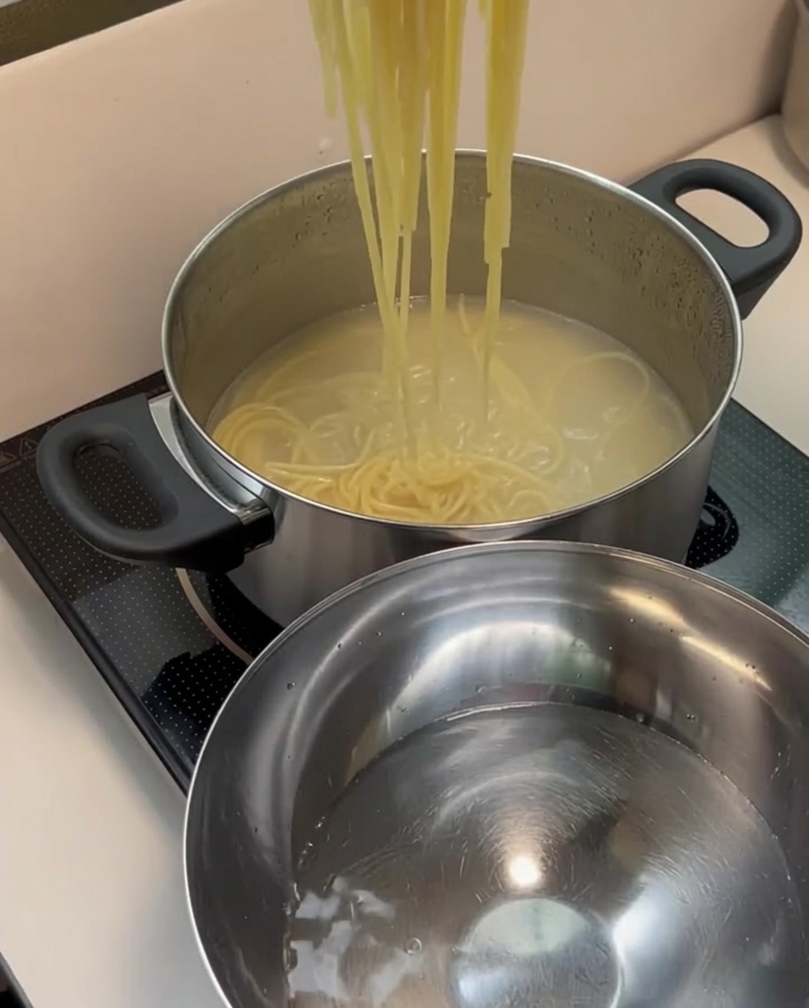 Spaghetti cotti scolati e trasferiti in una ciotola con acqua fredda.