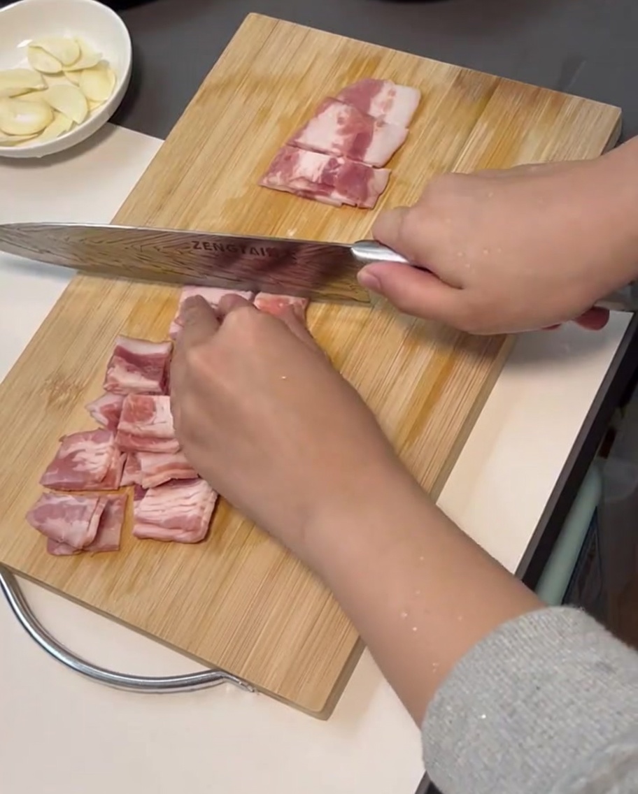 Strisce di pancetta tagliate a cubetti uniformi su un tagliere.