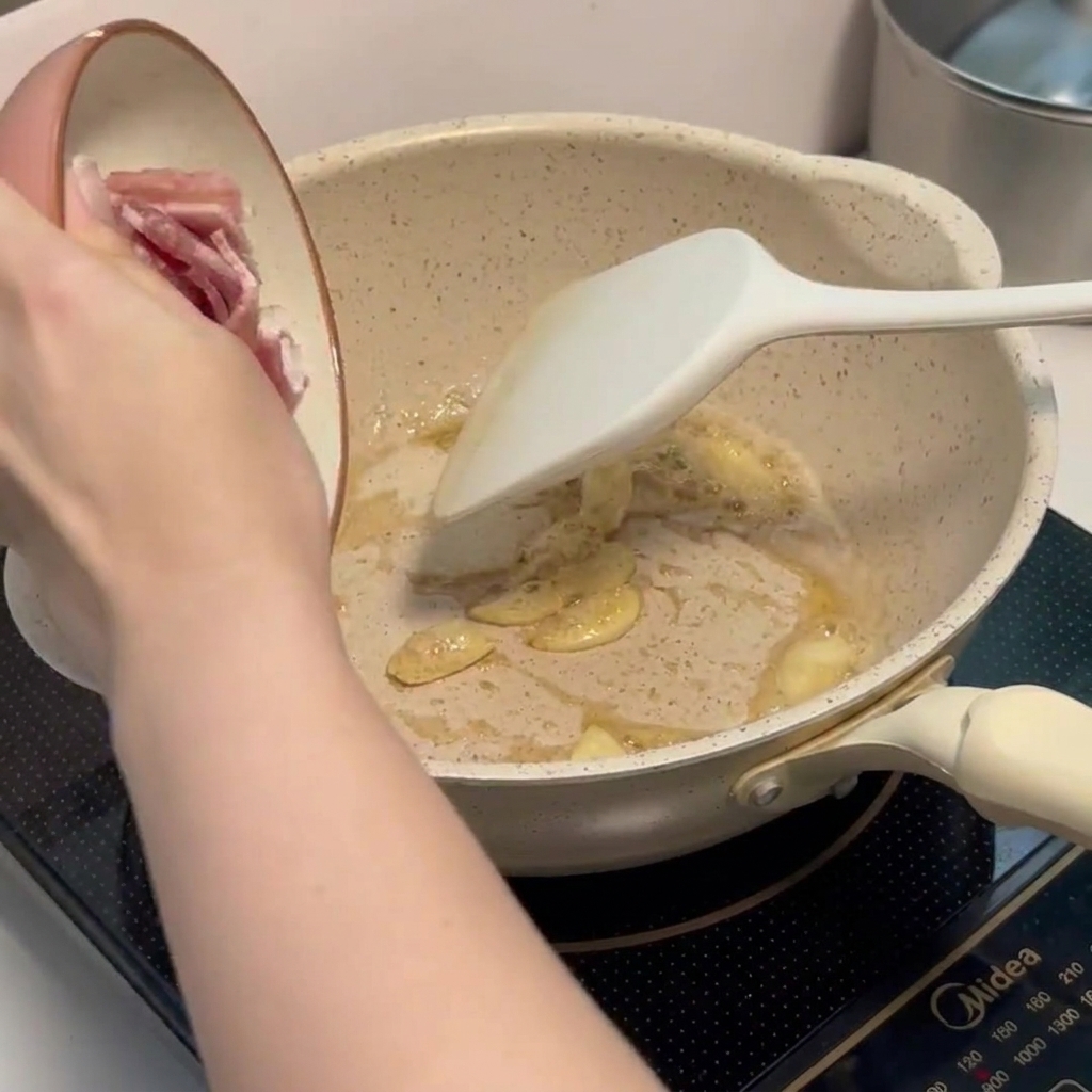 Pezzetti di pancetta che sfrigolano in padella con laglio.
