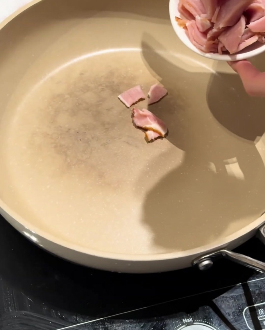 Pezzetti di pancetta magra che sfrigolano in una padella calda e asciutta, iniziando a rilasciare il grasso.