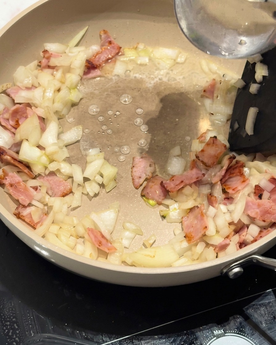Pasta riccioli inserita nella padella sopra la base di pancetta e cipolla.