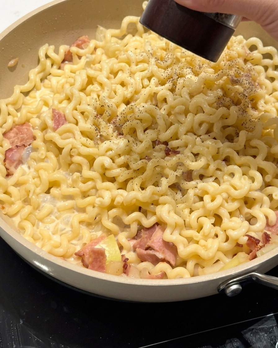 Pinze che mescolano la pasta cremosa nella padella con la salsa e la pancetta.
