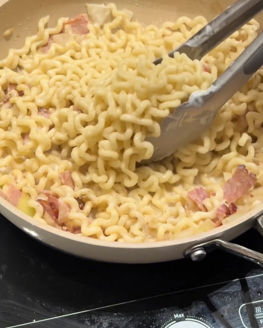 Parmigiano grattugiato cosparso sopra una padella di pasta carbonara cremosa.