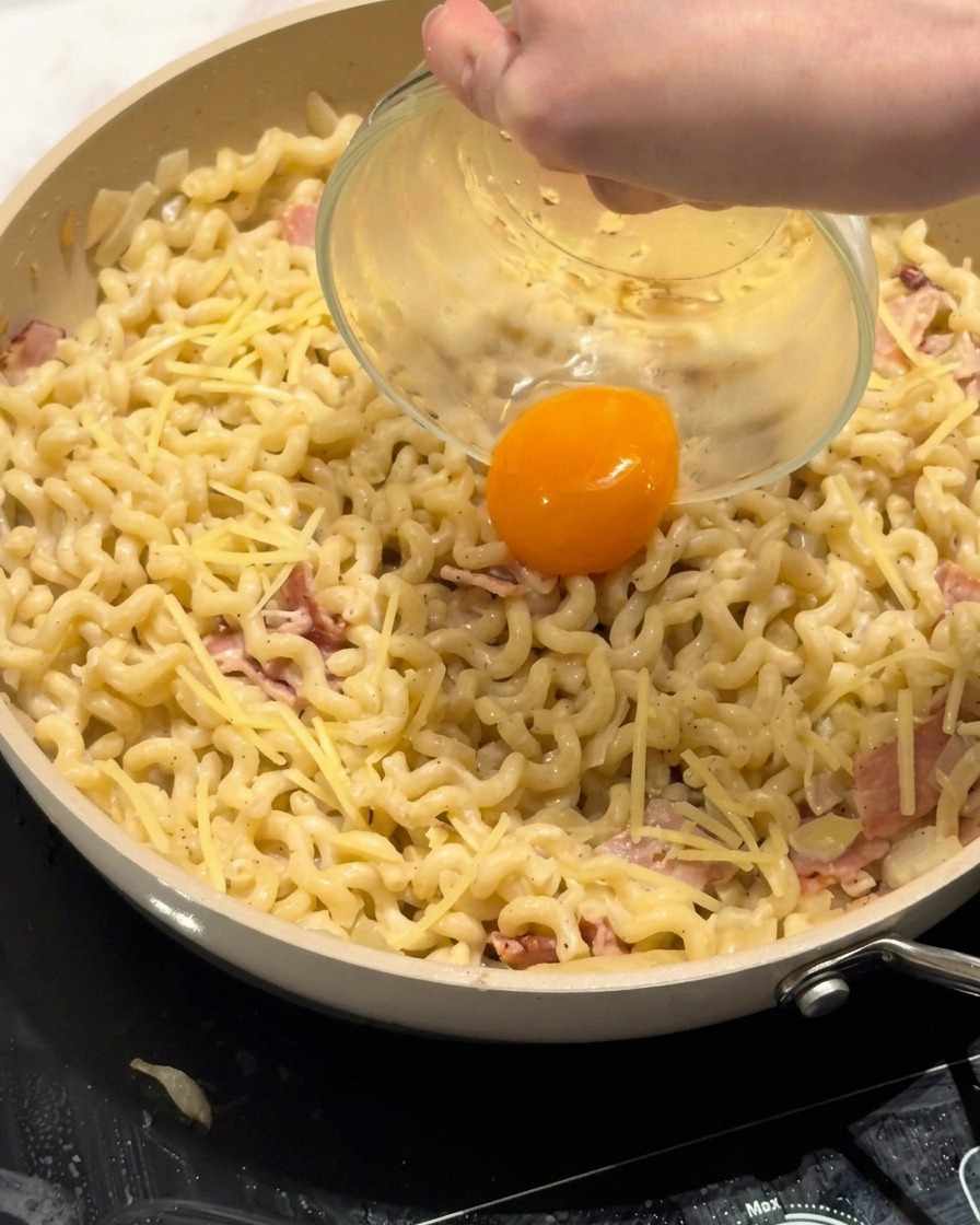 Un tuorlo duovo fresco posizionato al centro del piatto di pasta cremosa.