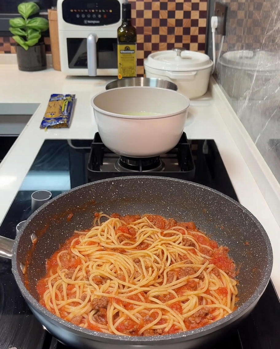 Una padella con spaghetti al ragù coperti da alcune fette di formaggio giallo.