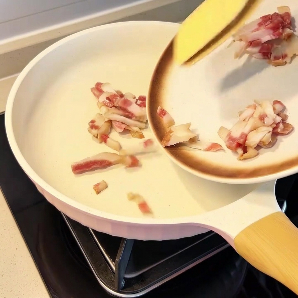 Pezzi di guanciale distribuiti uniformemente in una padella fredda.