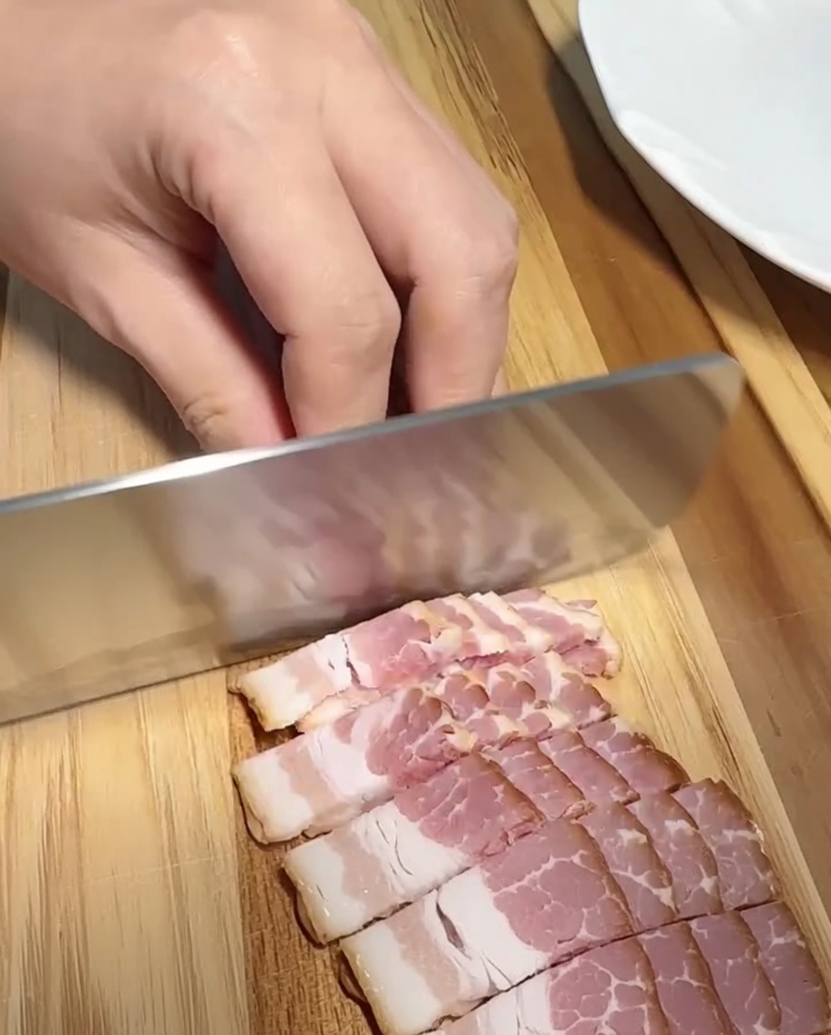 Un primo piano di fette di pancetta tagliate a pezzetti uniformi su un tagliere di legno.