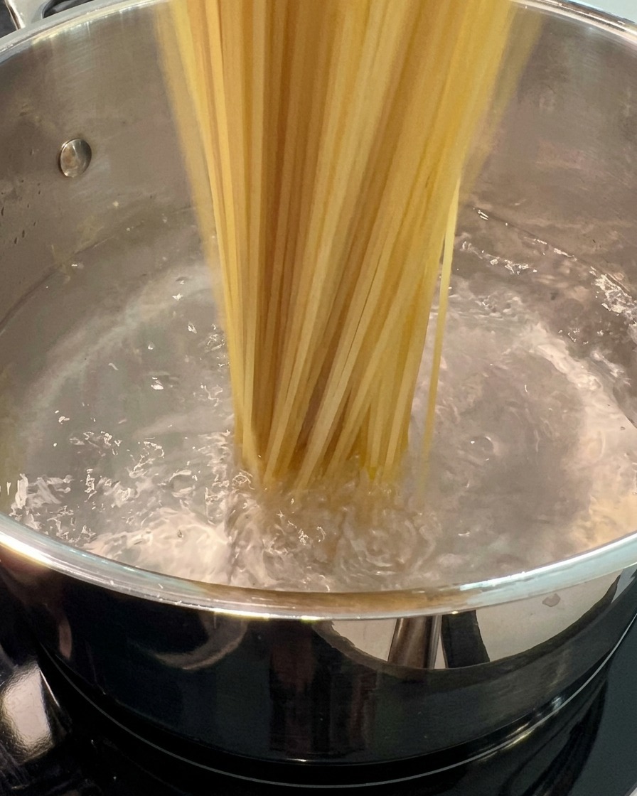 Spaghetti secchi immersi in una grande pentola di acqua bollente.