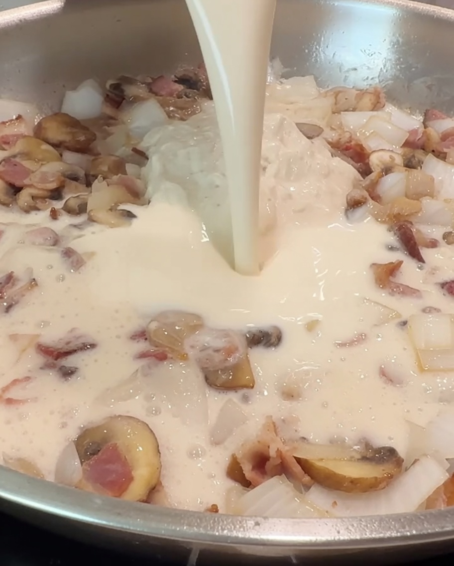 Una tazza di latte versata nella padella per amalgamarsi con la salsa Alfredo e gli ingredienti saltati.