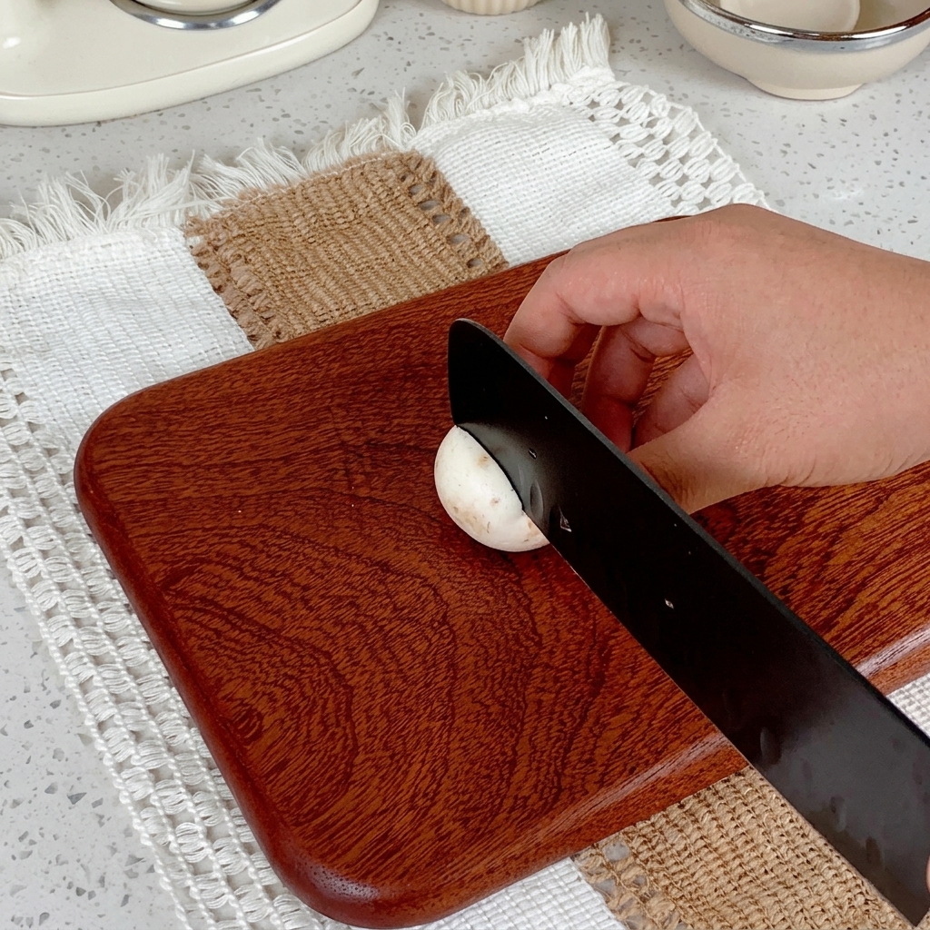 Una mano usa un coltello nero per affettare un fungo champignon su un tagliere di legno.